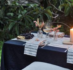 a table set with wine glasses, plates and napkins on it in front of trees