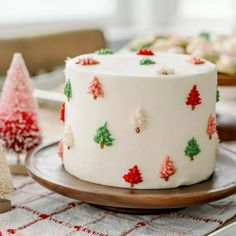 a decorated christmas cake sitting on top of a wooden platter next to small trees