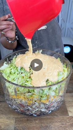 a person pouring dressing onto a salad in a bowl