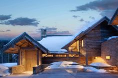 a house that has snow on the ground and lights in front of it, at dusk