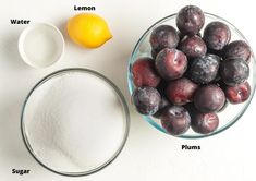 plums, lemon and sugar in bowls next to measuring cups on a white surface