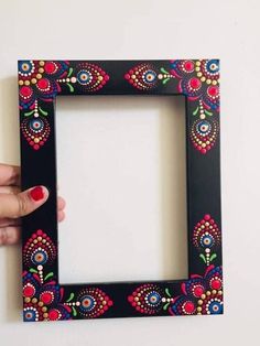 a hand holding up a black frame with colorful flowers on the front and bottom half