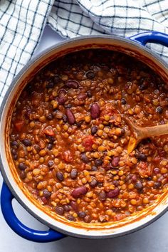 a blue pot filled with beans on top of a white tablecloth next to a wooden spoon