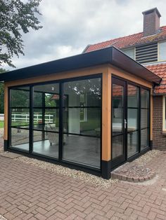 a small house with glass walls and doors on the outside, in front of a brick building