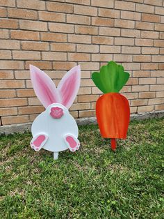 two plastic carrots sitting next to each other on the grass in front of a brick wall