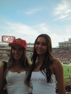 two beautiful young women standing next to each other in front of a crowd at a football game