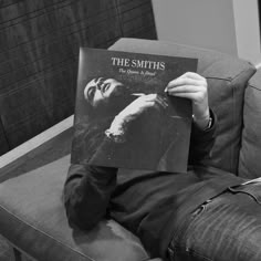 a man sitting on top of a couch holding up a book in front of his face