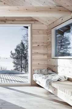 a bedroom with wooden walls and flooring next to a window overlooking the snow covered landscape