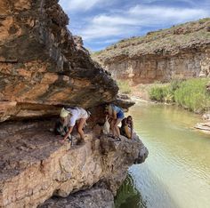 three people climbing up the side of a cliff next to a body of water with cliffs in the background