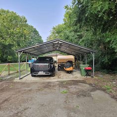 a black truck parked in front of a metal carport covered with tarp next to trees