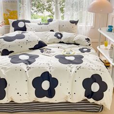 a bed with black and white flowers on it in front of a window next to a lamp