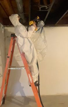 a man in white coveralls and safety equipment on a ladder working on a ceiling