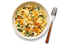 a white bowl filled with macaroni and cheese next to a fork on a white surface