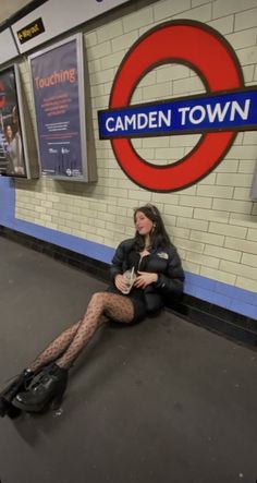 a woman sitting on the ground in front of a london train station with her legs crossed