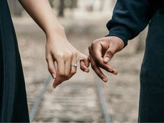 two people holding hands while standing on train tracks