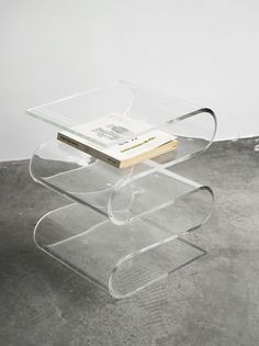 a clear table with a book on it and a white wall in the back ground