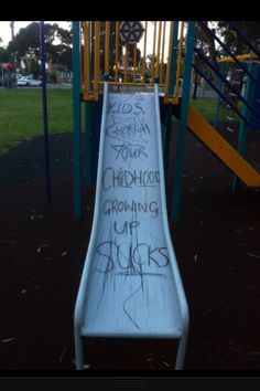 a slide with graffiti written on it in a park area next to a play structure