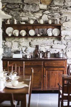 a dining room table with plates and cups on it, next to a stone wall