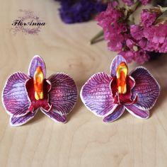 two purple flowers sitting next to each other on top of a wooden table with pink and purple flowers in the background