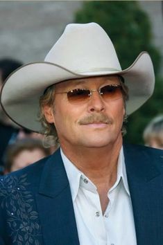 a man in a cowboy hat and sunglasses looks at the camera while standing next to other people