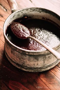 an old metal pot filled with liquid on top of a wooden table next to a spoon