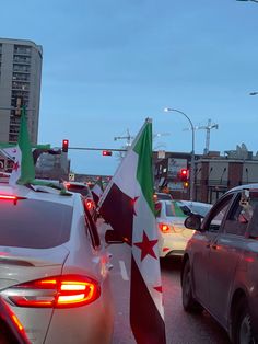 several cars are driving down the street with flags on their hoods and tail lights