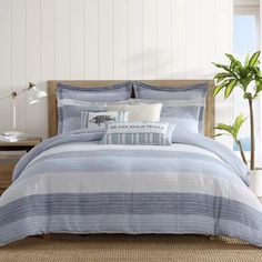 a bed with blue and white striped comforter in a room next to a potted plant