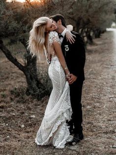 a bride and groom kissing in the middle of an olive tree lined road at sunset