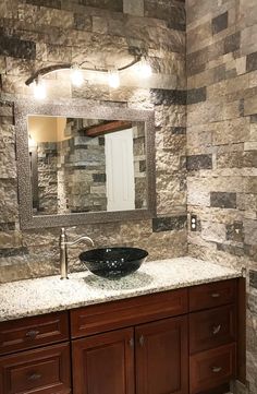 a bathroom sink sitting under a mirror next to a wooden cabinet and counter top in front of a stone wall