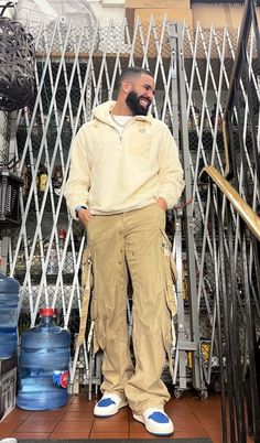 a man with a beard standing in front of a metal gate and holding his hands on his hips