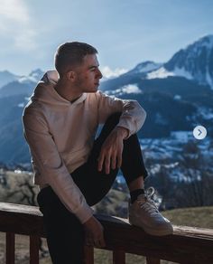 a man sitting on top of a wooden bench in front of snow covered mountain range