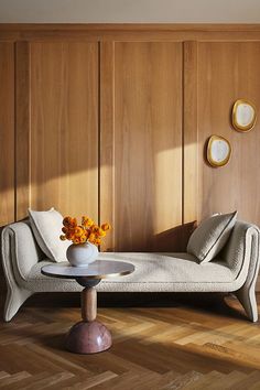 a white couch sitting next to a table with flowers in it on top of a hard wood floor