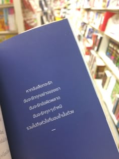 a person holding up a blue book in front of bookshelves filled with children's books