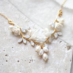 a gold necklace with white flowers and pearls hanging from it's side on a marble surface