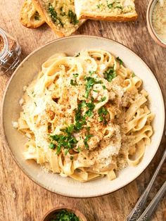 a plate of pasta with parmesan cheese and herbs on it next to two slices of bread