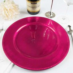 a table setting with pink plates, silverware and wine bottle on it for an elegant dinner