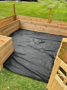 an outdoor play area made out of wood and black tarp, in the grass