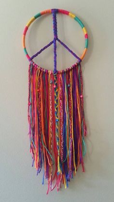 a peace sign hanging on the wall with multicolored beads and tassels