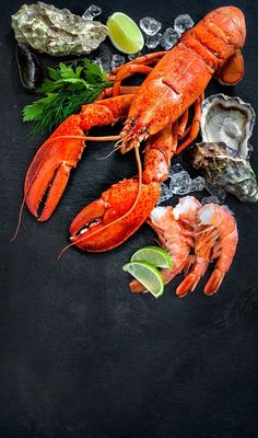 lobsters and oysters on a black surface with lime wedges, salt and pepper