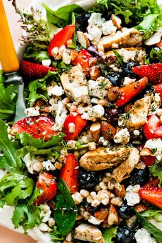 a salad with strawberries, chicken, feta cheese and nuts in it on a white plate