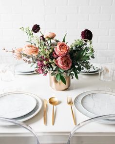 a table set with plates, silverware and flowers in a gold vase on it