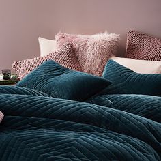 a bed with blue comforter and pillows on top of it in front of a pink wall