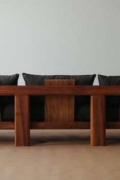 two wooden benches with black pillows on them in front of a white wall and floor