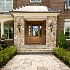 the front entrance to a brick home with stone walkways and potted plants on either side