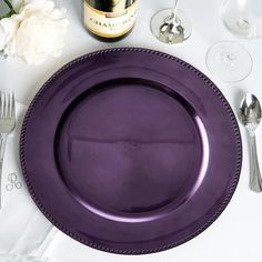 a purple plate sitting on top of a table next to wine glasses and silverware