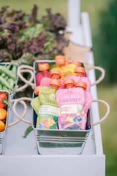 two metal trays filled with fruit and vegetables on a white tablecloth next to each other