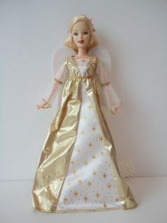 a doll dressed in gold and white with stars on it's dress, standing next to a wall