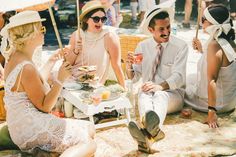 a group of people sitting on top of a blanket next to each other eating food