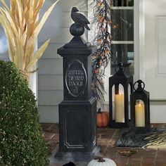 a black bird statue sitting on top of a post in front of a house with candles