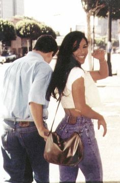 a man and woman walking down the street with one holding a handbag on her hip